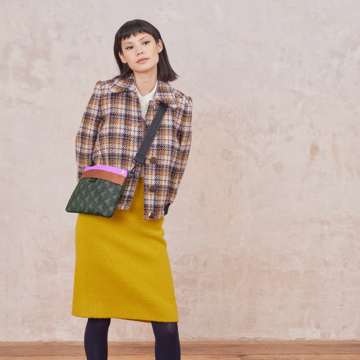Woman wearing a plaid jacket and yellow skirt with with a black and grey crossbody bag.