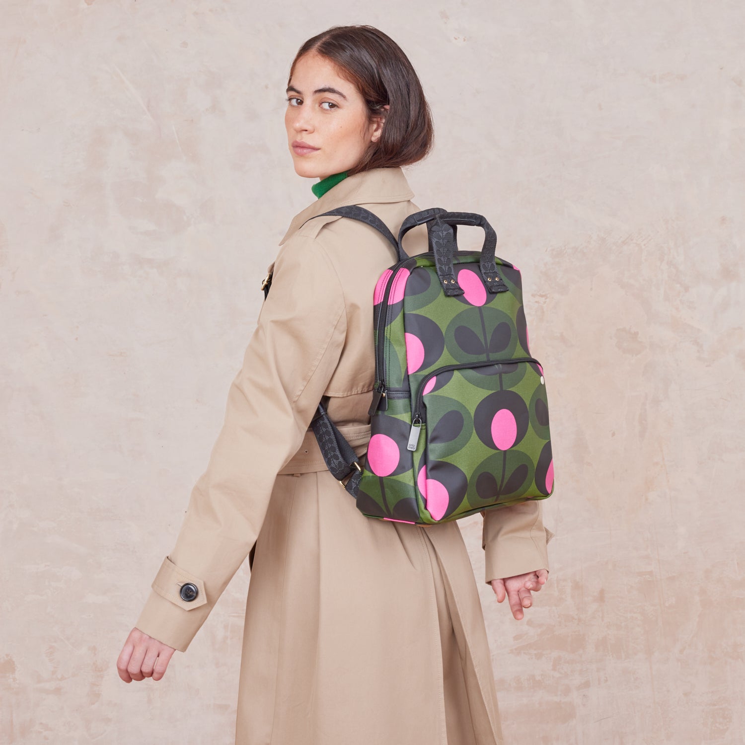 Woman wearing a the Lotta Backpack in a green stem print with bright pink dots, featuring branded grab handles and straps