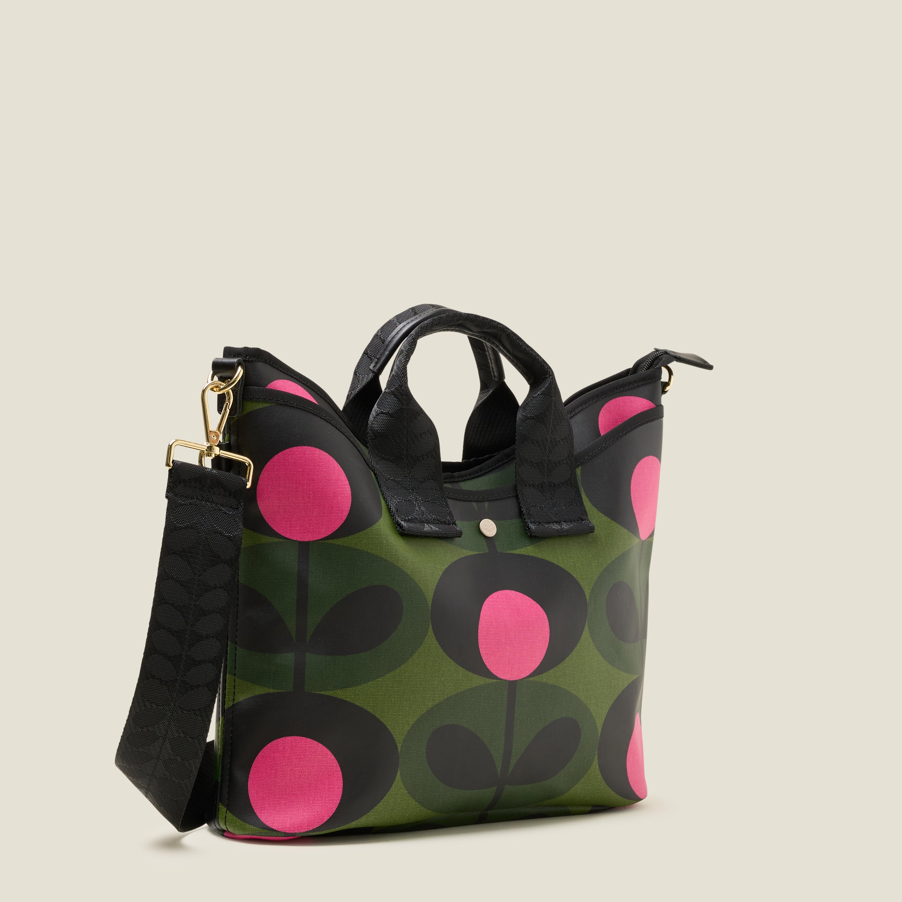 Side view of crossbody bag in forest green print with pink dots, featuring a front slip pocket and branded grab handles and detachable strap.