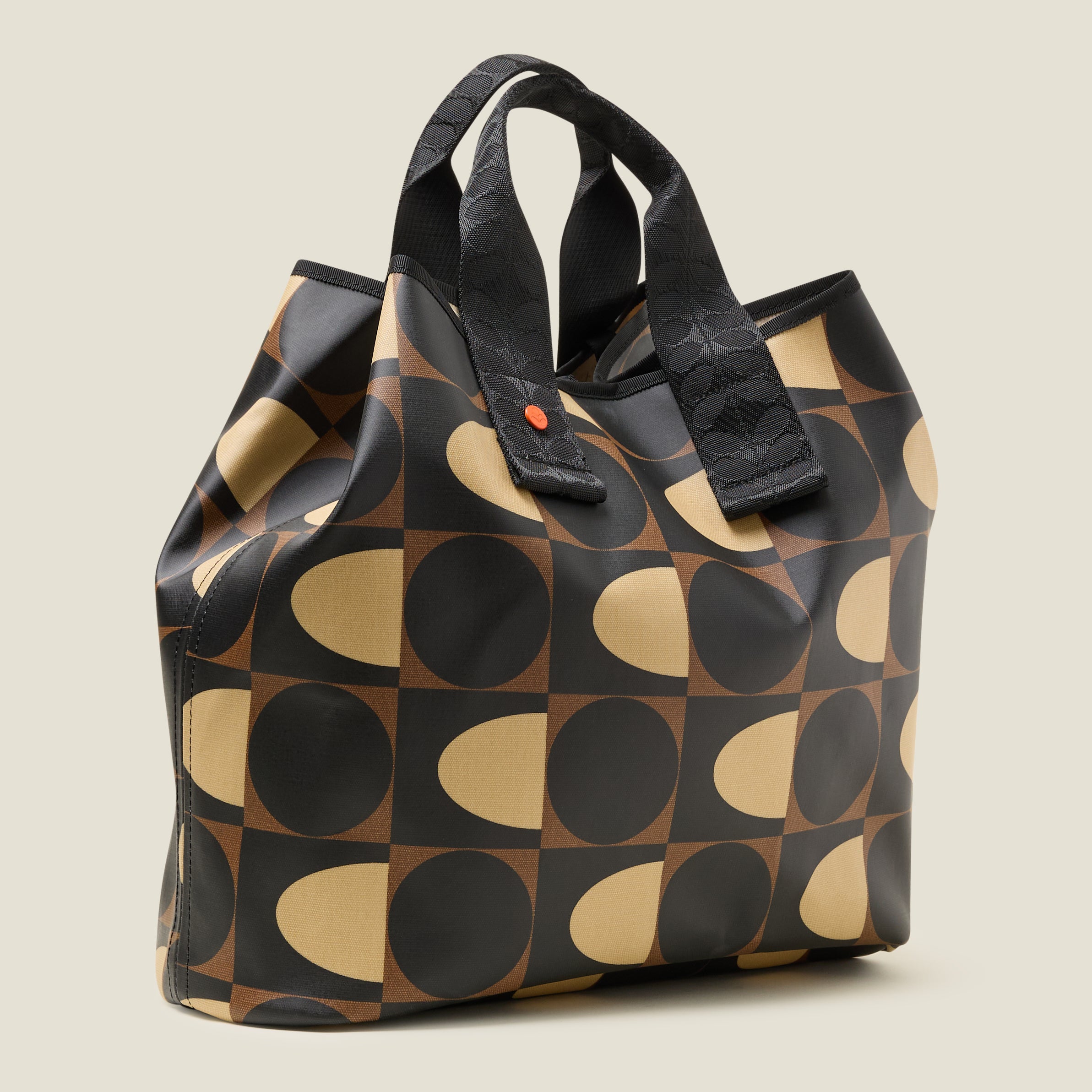 Side view of patterned tote bag with black, brown and beige spot square printed design, with top corners folded for more security, with two short grab handles. 