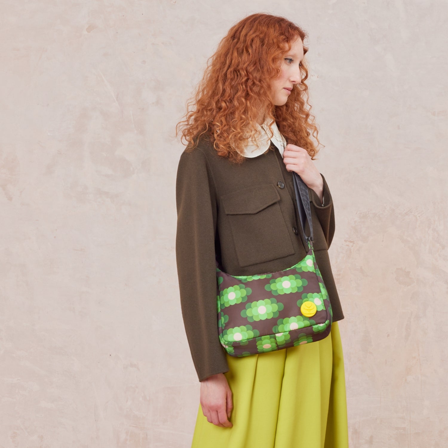 A woman wears the small crossbody hobo bag, in our neon green pattern with yellow stem logo branding.
